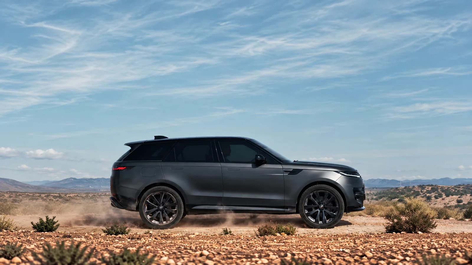 SUV preto atravessa uma estrada de terra em uma paisagem desértica, imagem ilustrativa